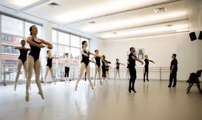 Ballet dancers taking class in a studio are mid-air